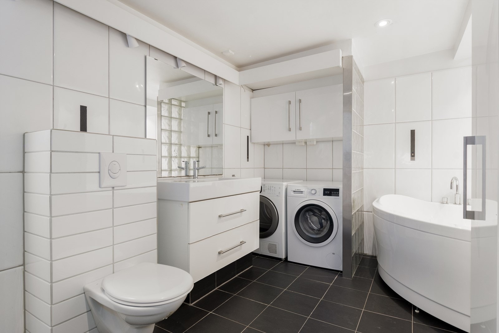 Stort, flislagt bad med varmekabler i gulv. Nisje for vaskemaskin og tørketrommel Galleribilde