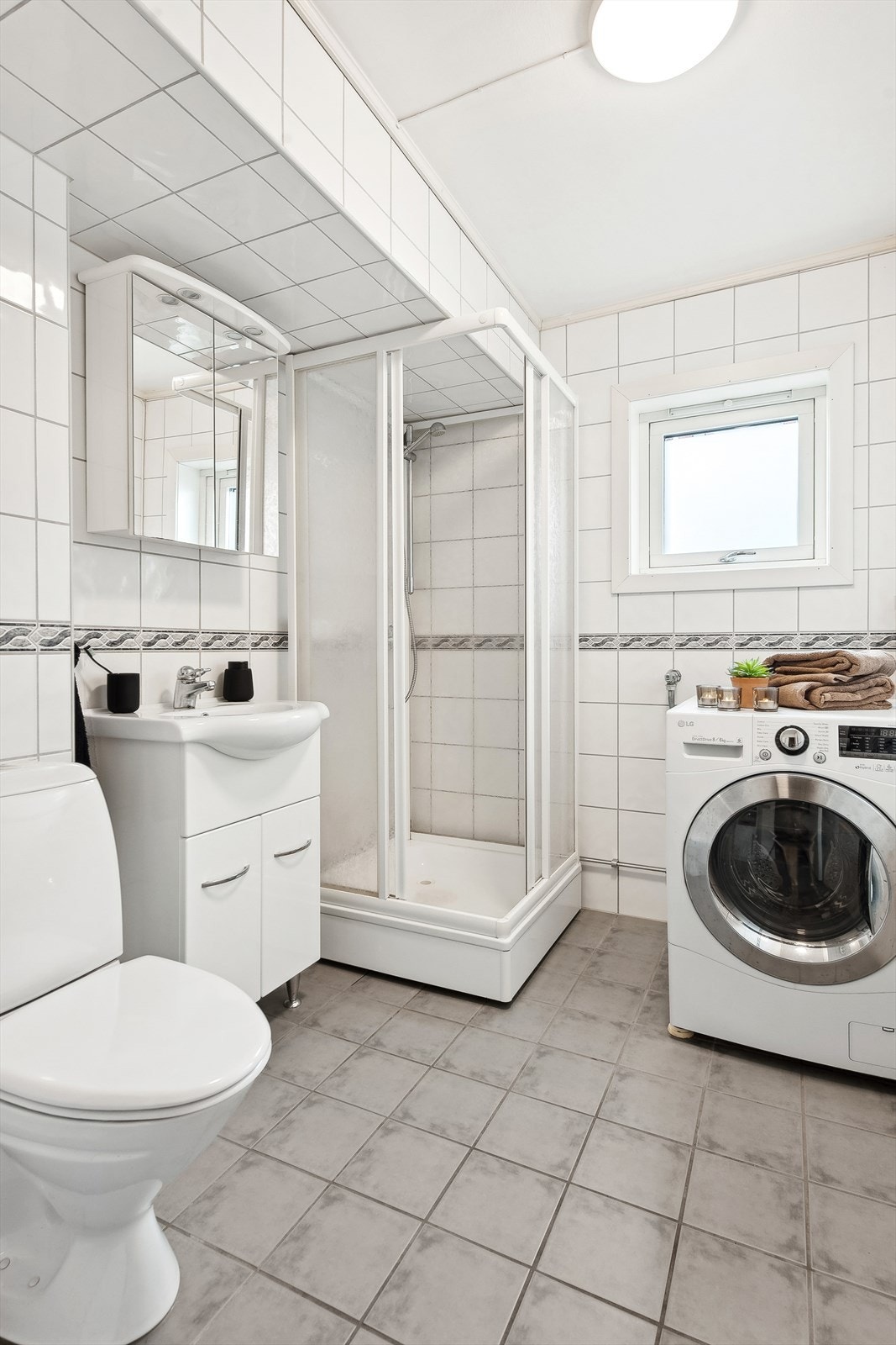 Komplett flislagt bad med servant, WC, dusjkabinett og opplegg til vaskemaskin. Galleribilde