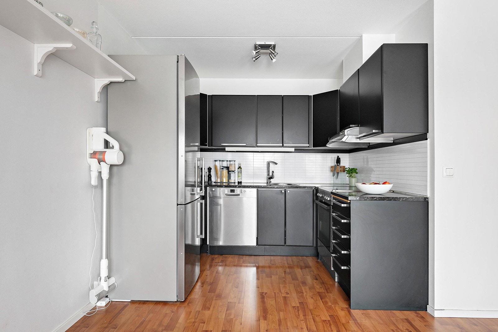 Kjøkkeninnredning med slette fronter, benkeplate av laminat, nedfelt oppvaskkum med ett-greps armatur, belysning og stikkontakter under overskap samt frittstående hvitevarer Galleribilde