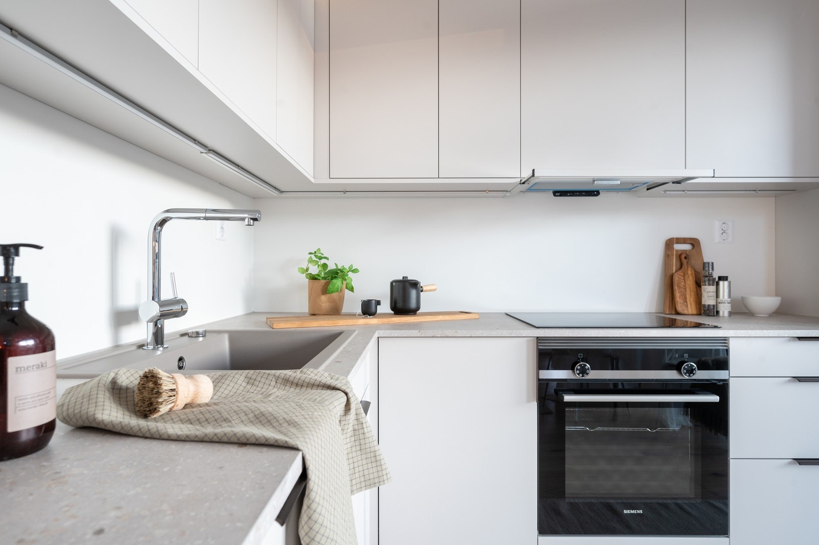 Kjøkkenet er vinkelformet og tilpasset den åpne løsningen til stuen. Innredningen har lysegrå slette kjøkkenfronter med sorte håndtak og grå laminert benkeplater. Galleribilde