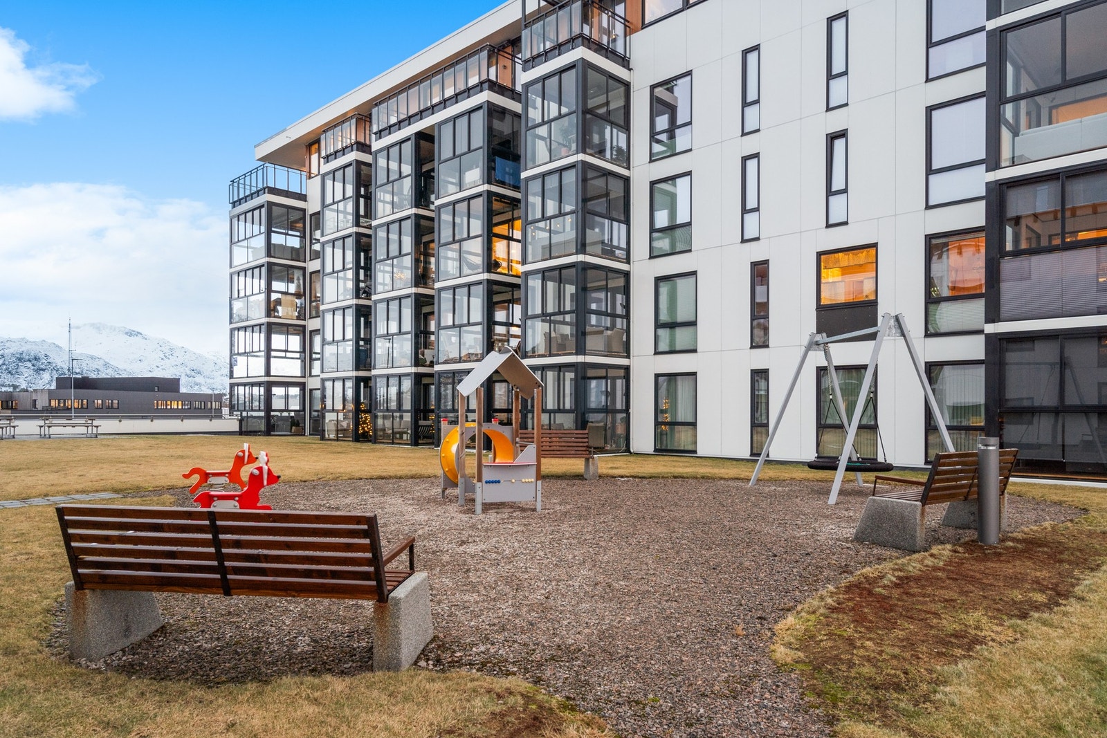 Pent opparbeidet uteområde med lekeplass, gressplen og benker. Galleribilde