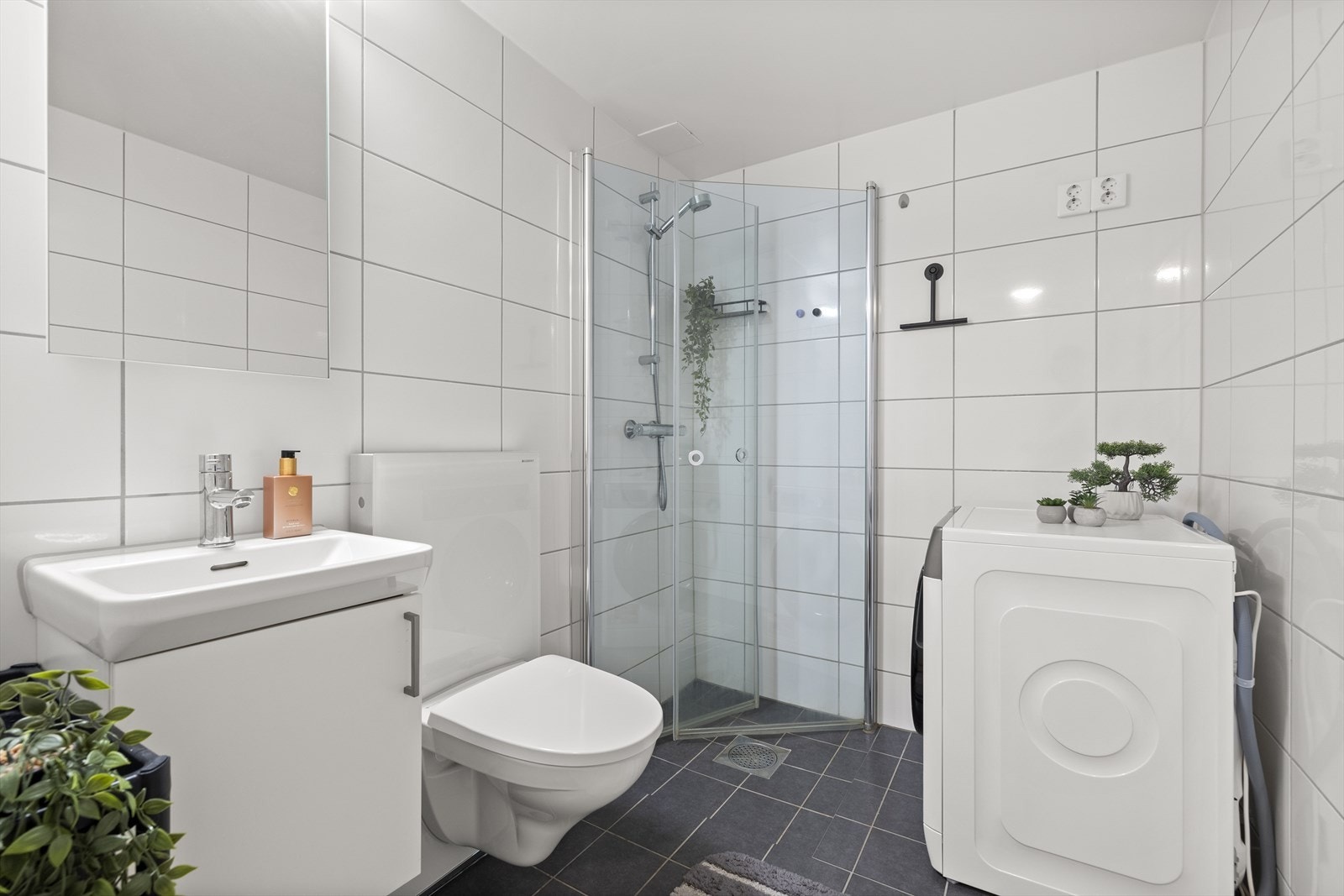 Badet er lyst og pent flislagt, og har servant med møbel og speil, dusjhjørne, vegghengt toalett og opplegg for vaskemaskin. Galleribilde