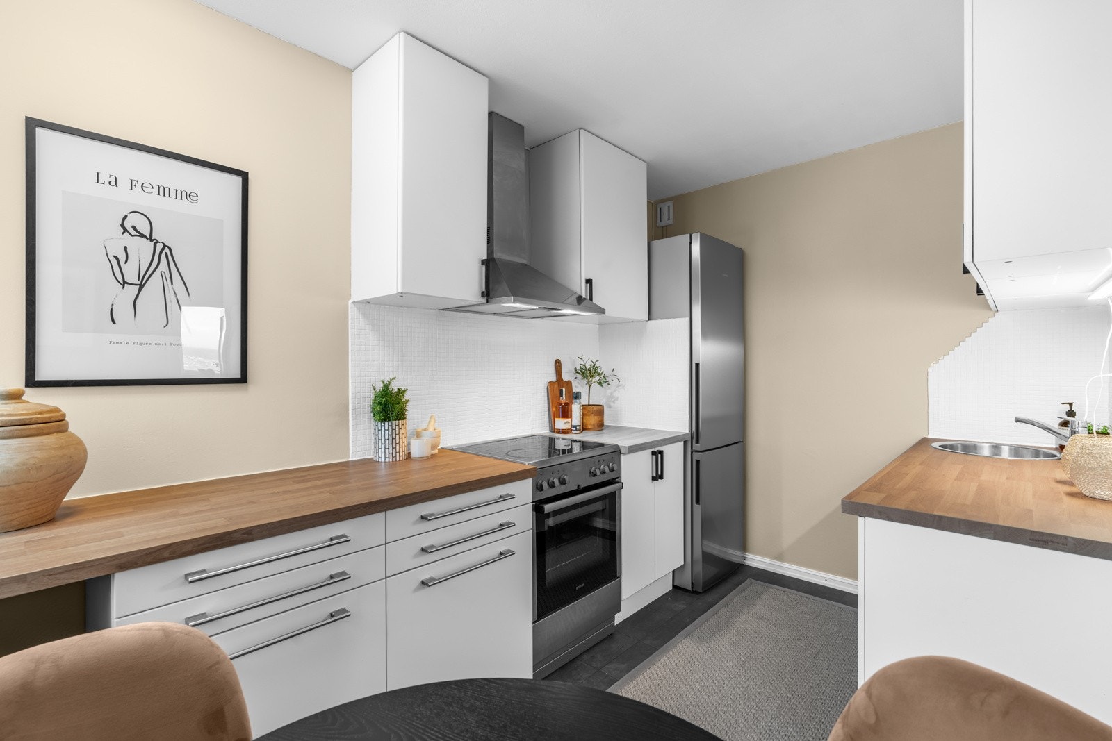 Innredningen har hvite, glatte fronter, takhøye skap og en pen benkeplate i laminat fra 2025 med nedfelt kum i stål. Galleribilde