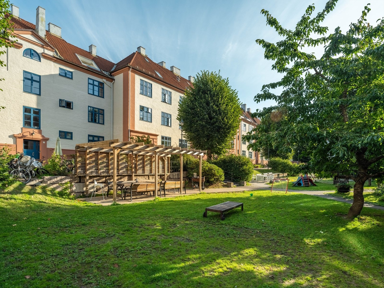 Idyllisk gårdsrom med plen, beplantning, sittegrupper og lekeplass. Galleribilde