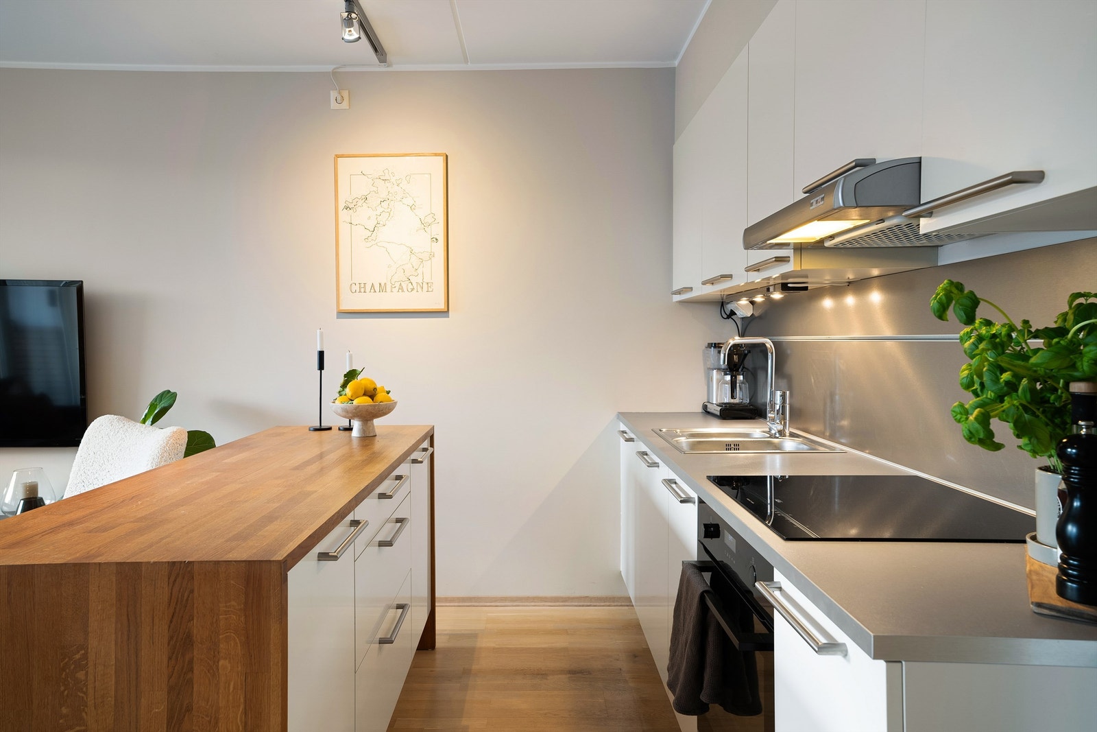 Kjøkken fra HTH med glatte fronter, benkeplate av laminat og tre, dobbel oppvaskkum av rustfritt stål med ett-greps armatur, benkeskapsbelysning og stikkontakter under overskap. Galleribilde