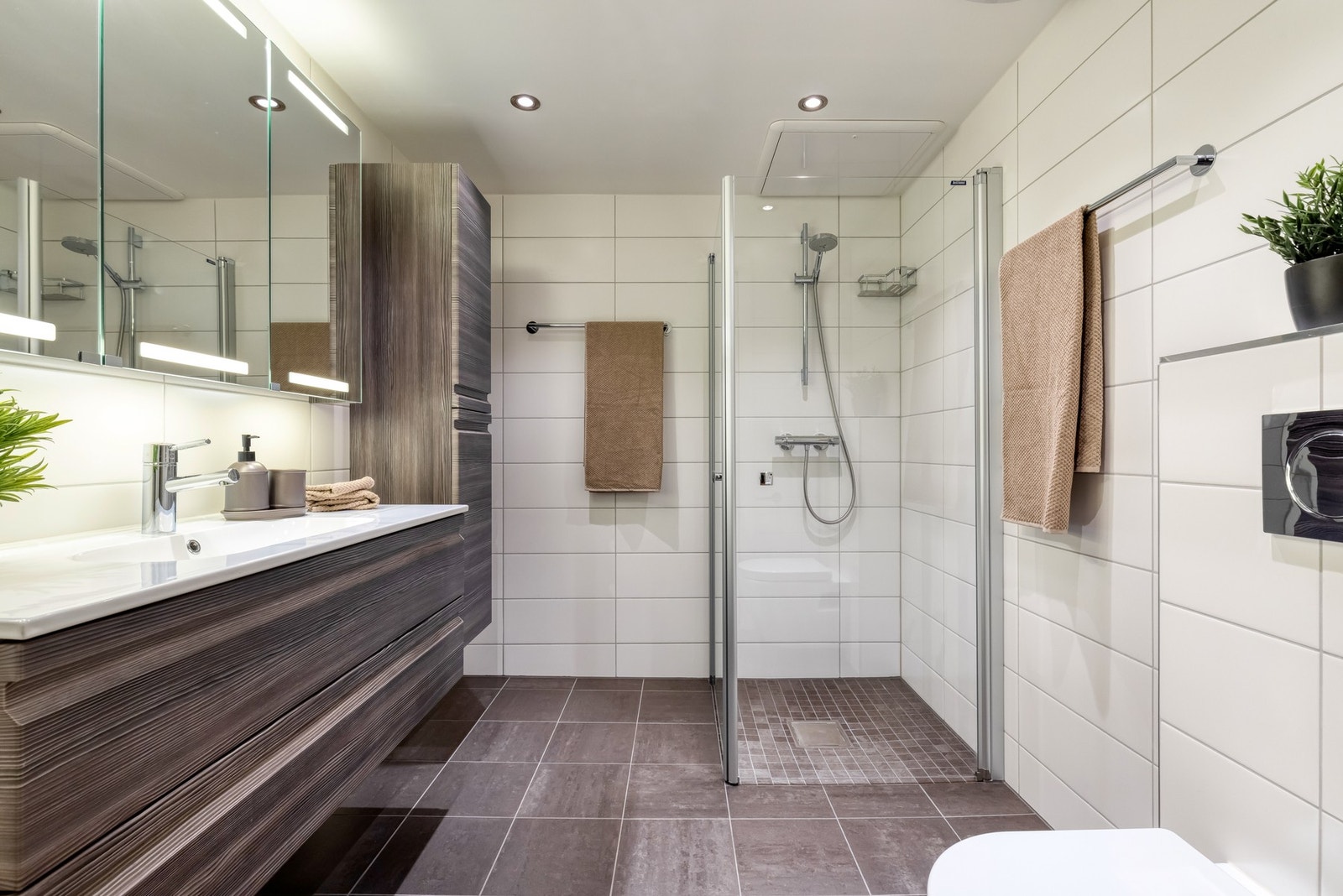 Badet fra hovedsoverommet er romslig og tidløst innredet med grå gulvfliser og hvite fliser på veggene Galleribilde