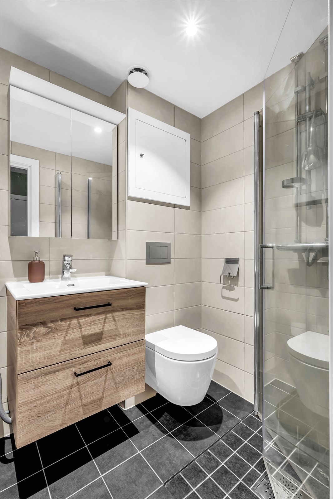 Badet har varmekabler på gulv, praktisk dusjhjørne, vegghengt toalett, servant med oppbevaring og opplegg for vaskemaskin (smal type). Galleribilde