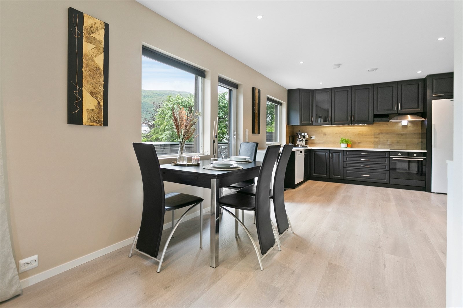 Kjøkkeninnredning i laminat med malte, profilerte fronter. Det er ventilatorhette over integrert komfyr, opplegg for oppvaskmaskin, laminat mellom benk og overskap. laminat benkeplate med nedfelt oppvaskkum. Galleribilde