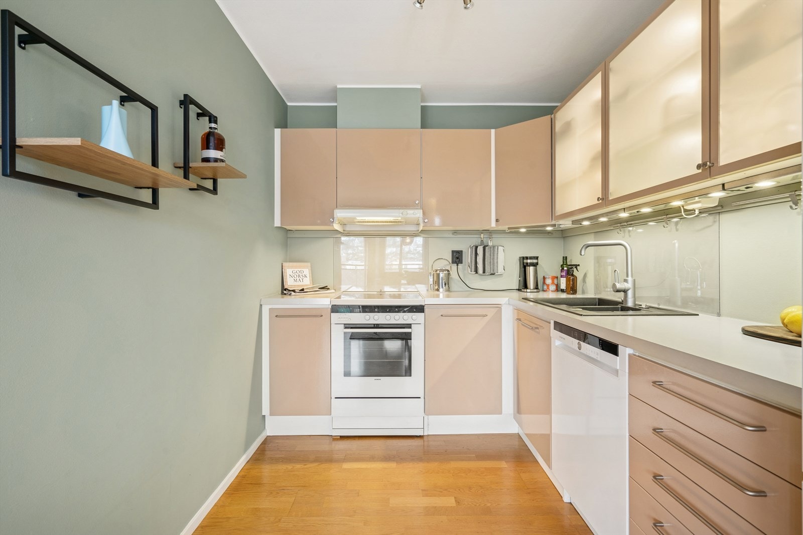 Kjøkkeninnredning med glatte folierte fronter, vitrinedører med frostet glass og innvendig belysning samt laminat benkeplate. Galleribilde