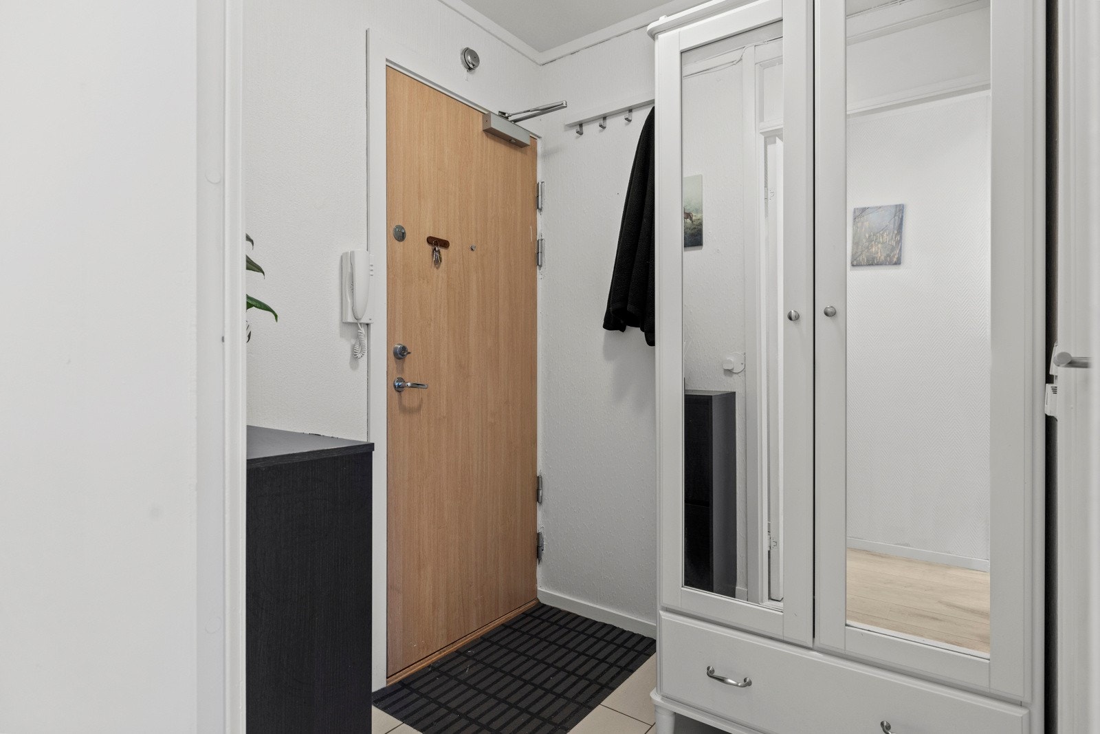 Entreen er innredet med grå gulvfliser og en porttelefon ved ytterdøren Galleribilde