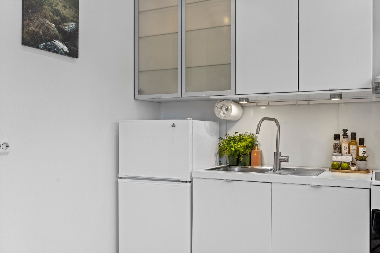 Innredningen har hvite, glatte fronter og benkeplate av laminat, samt hvitevarer som komfyr og en kombinert kjøl/frys tilpasset innredningen Galleribilde