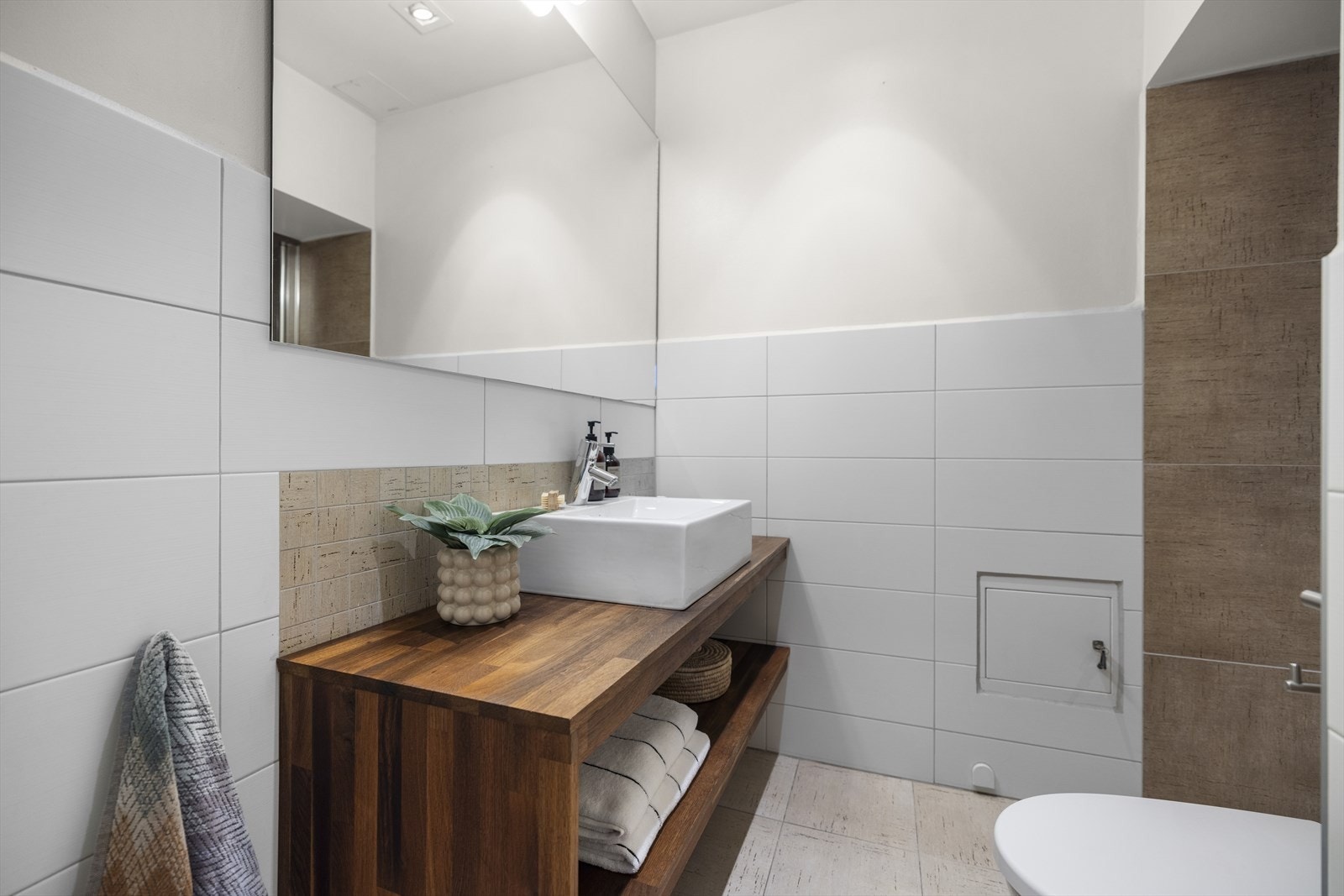 Tidløst bad med flislagte vegger og gulv med elektriske varmekabler. Badet er innredet med plassbygd baderomsinnredning i heltre med en toppmontert servant i keramikk, kromfarget blandebatteri og et stort speil med veggbelysning over Galleribilde