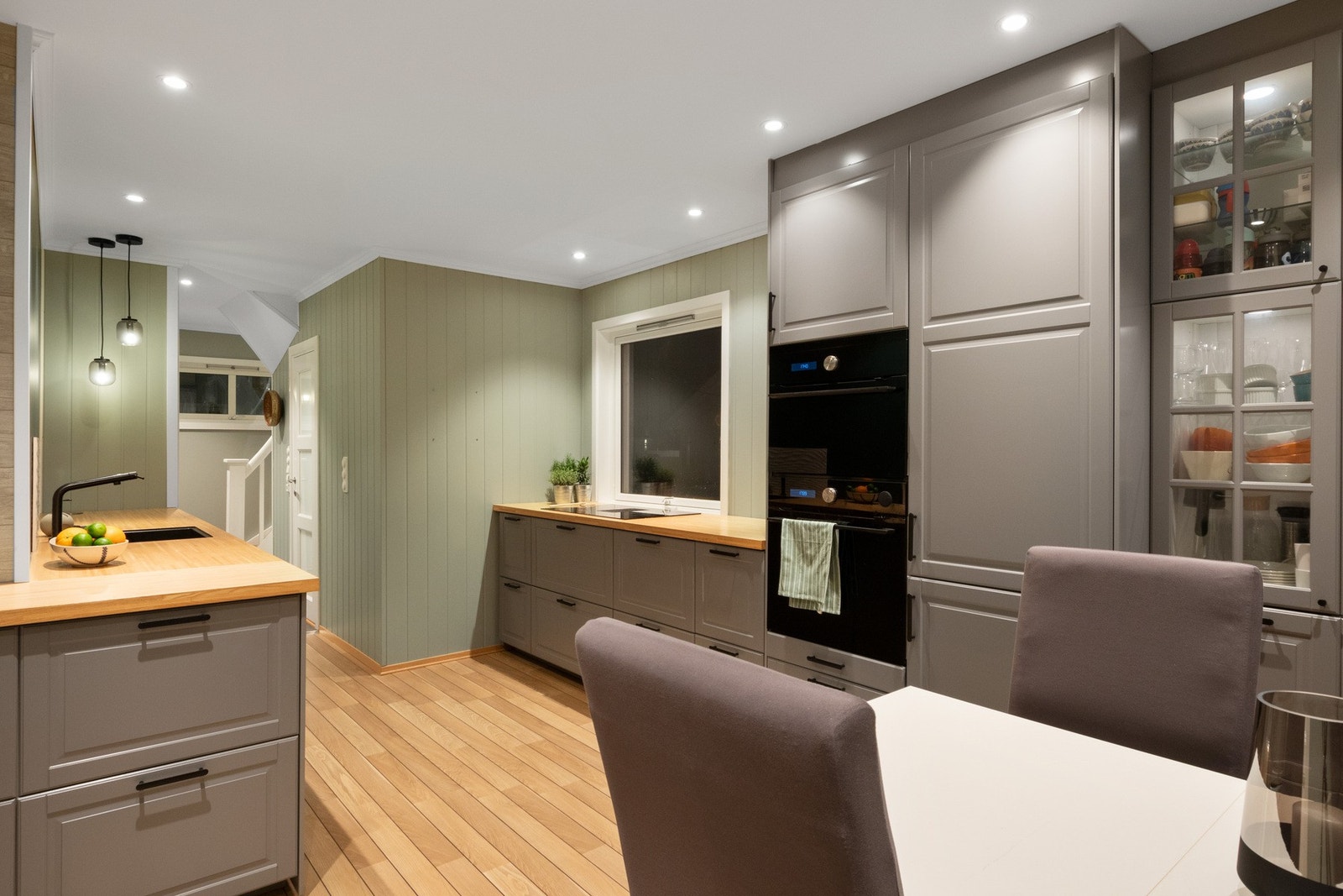 Innredningen har grå, profilerte fronter, vitrinedører, takhøye skap og heltrebenkeplate med planlimt, sort kum. Galleribilde