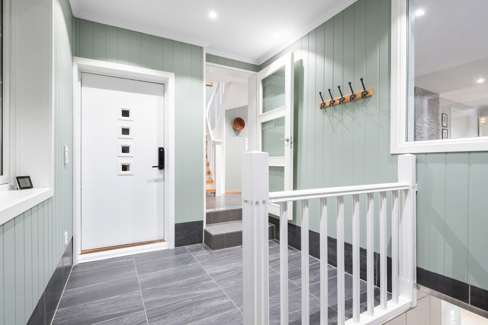 Fin entré med lys grønn panel på veggene, downlights i himlingen og grå fliser på gulv med gulvvarme. Galleribilde