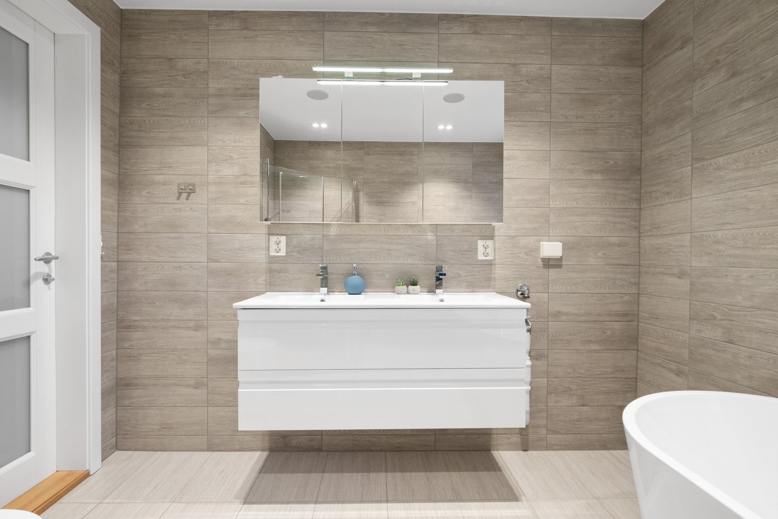 Baderomsinnredningen har hvite fronter og består av en heldekkende dobbelservant på en skuffeseksjon og et bredt speilskap med belysning. Galleribilde