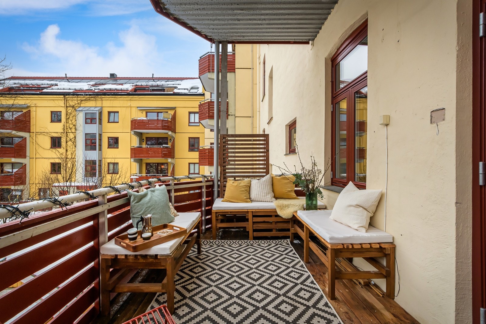 Balkongen har terrassebord på gulv, rekkverk med trekledning og utvendig stikkontakt montert på vegg. Galleribilde