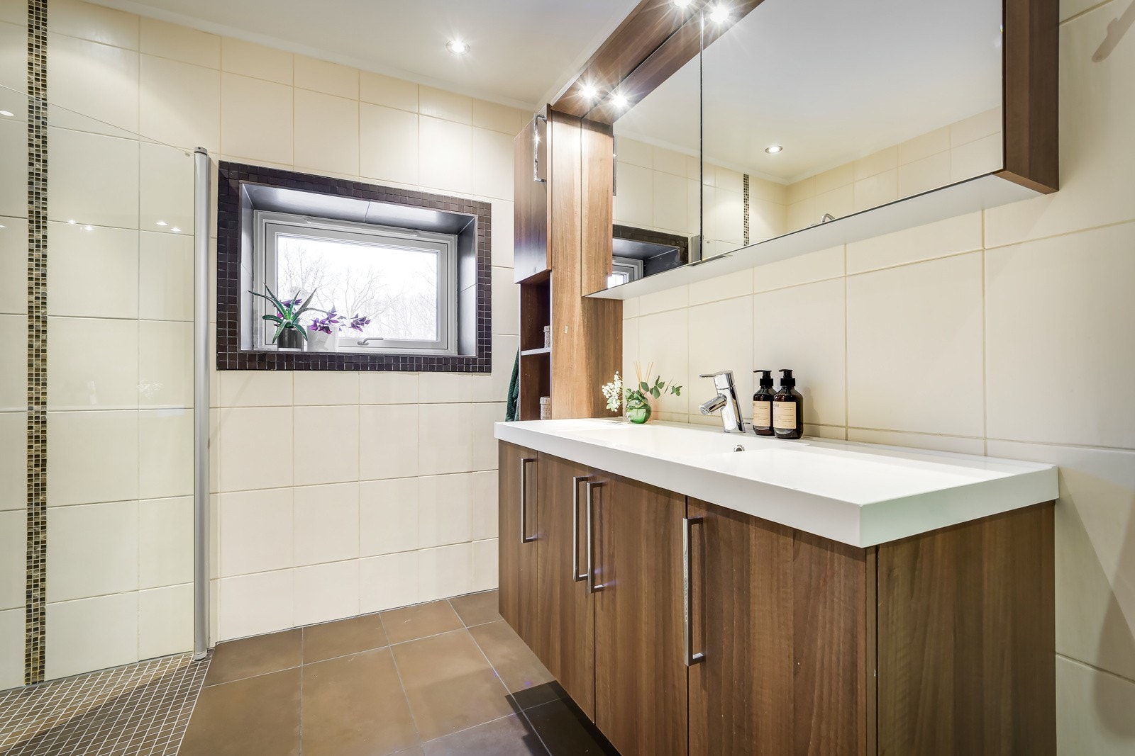 Flott baderomsinnredning med glatte fronter og heldekkende servant, speilskap med belysning over og ekstra høyskap ved siden av. Galleribilde