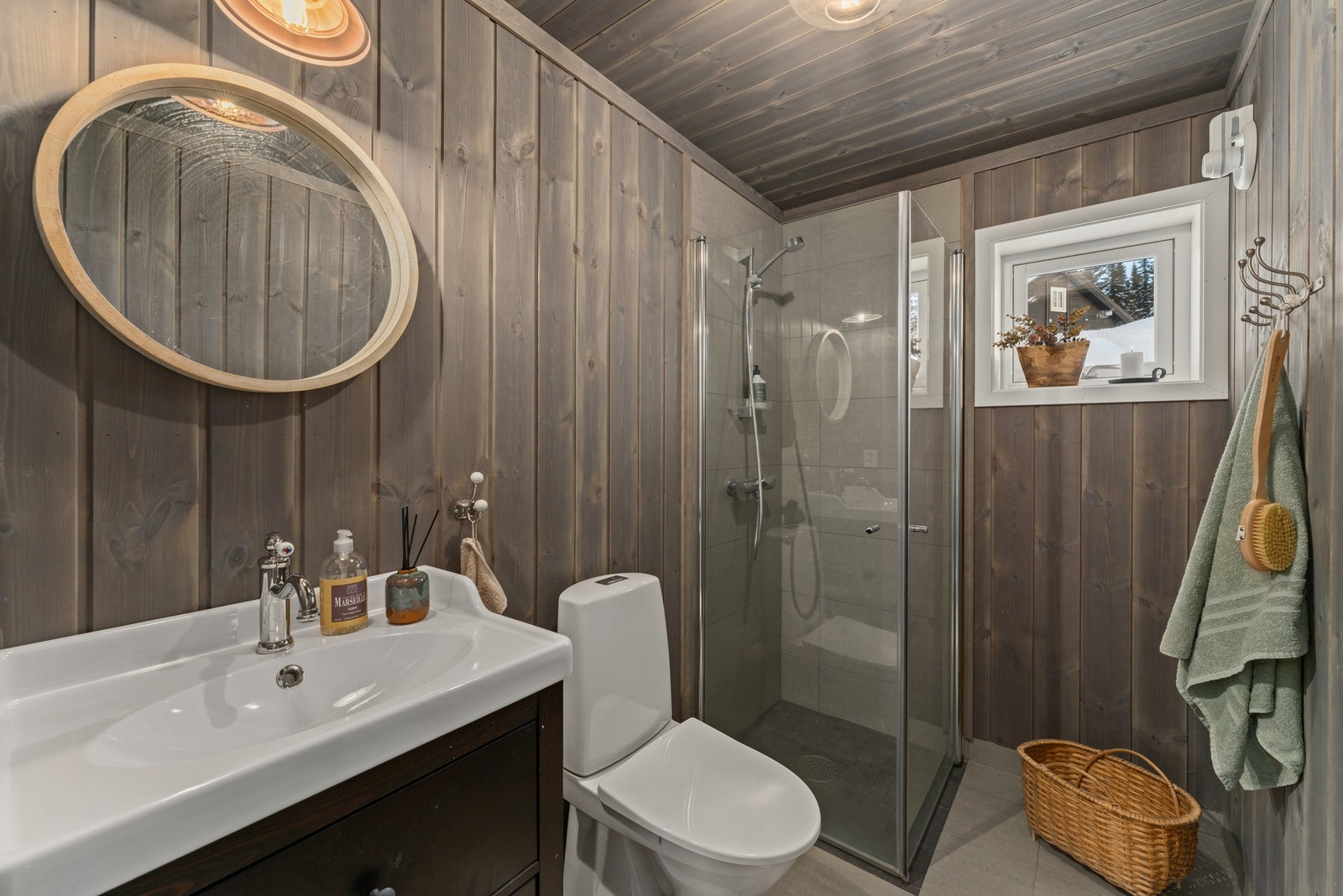 Badet har panelvegger og -tak i naturlig treverk, samt en dusjnisje med glassdører. Det er et vindu som slipper inn dagslys, og en moderne servant med underskap og speil over. Galleribilde