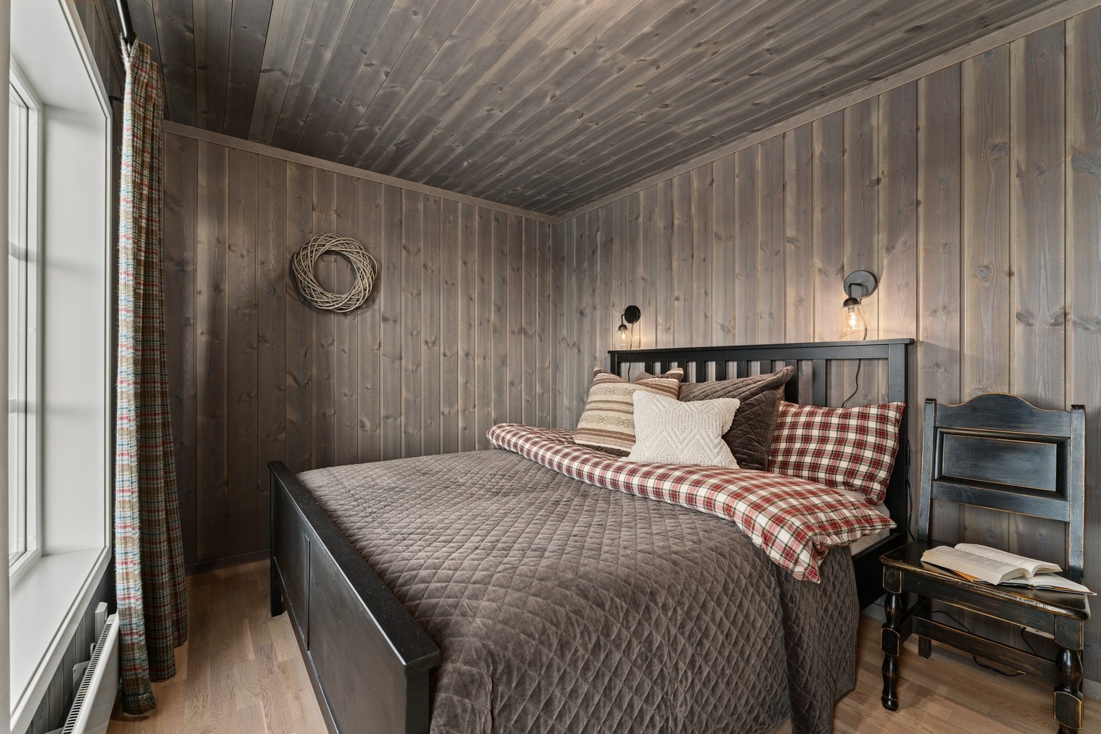 Soverommet har panelvegger og tak i mørkt tre, med store vinduer som slipper inn naturlig lys. Rommet har en koselig atmosfære med varme farger og teksturer. Galleribilde