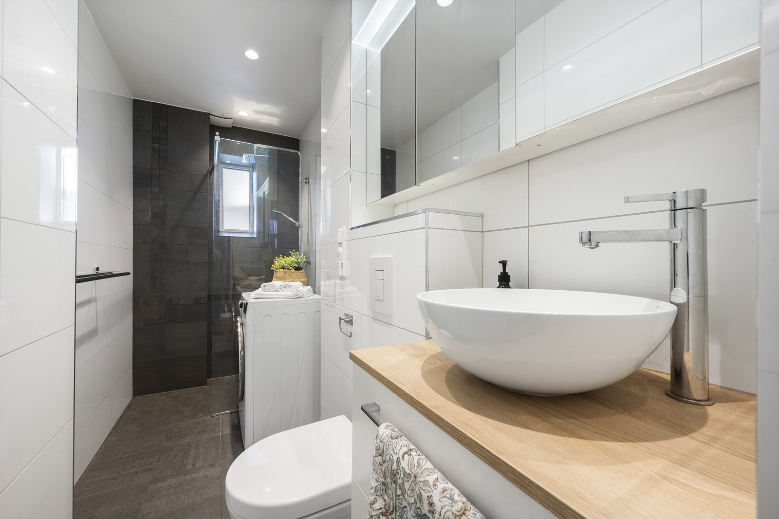 Badet er innredet med vegghengt klosett, servant på innredning, speilskap og dusjhjørne med glassfelt. Galleribilde