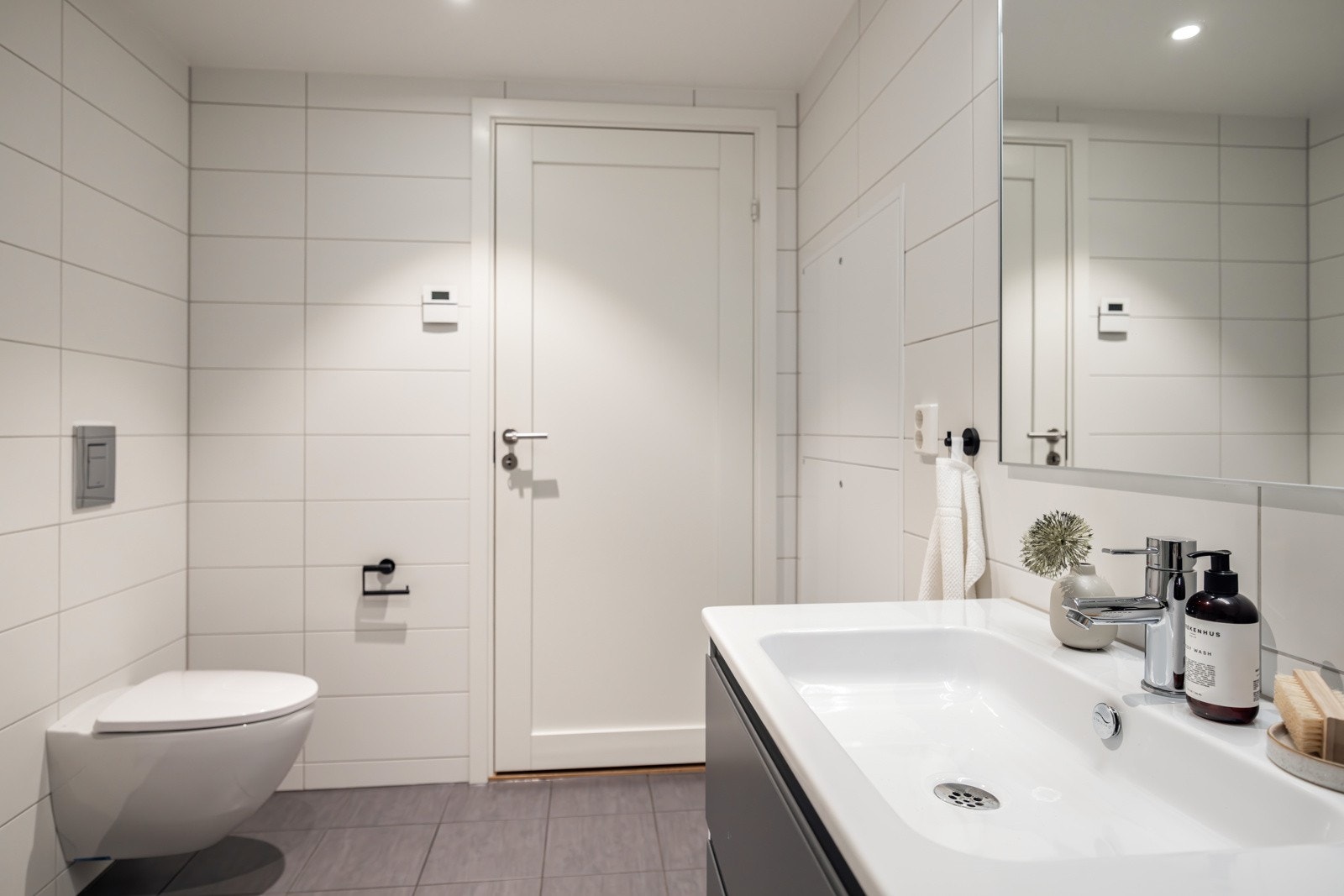 Romslig dusjhjørne med innfellbare rette dusjdører i glass og vegghengt toalett med skjult sisterne. Galleribilde