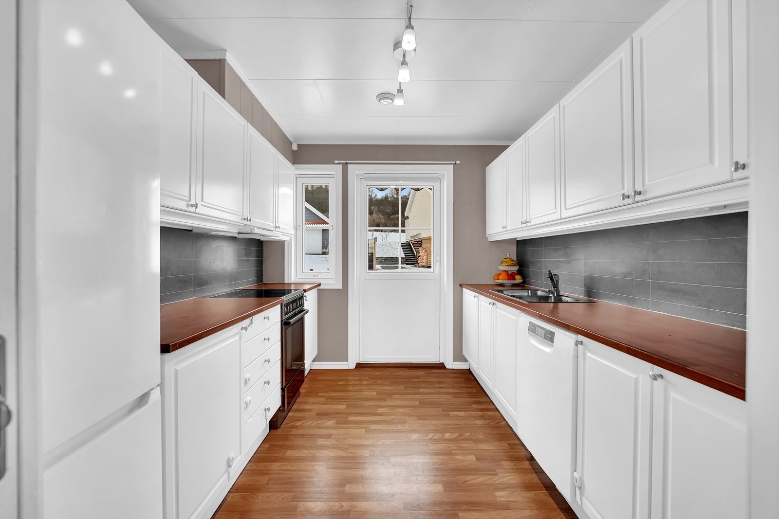 Velholdt og tidløst kjøkken i eget rom - Innredning har profilerte fronter, benkeplate i lamiant og avsatt plass til hvitevarer. Galleribilde