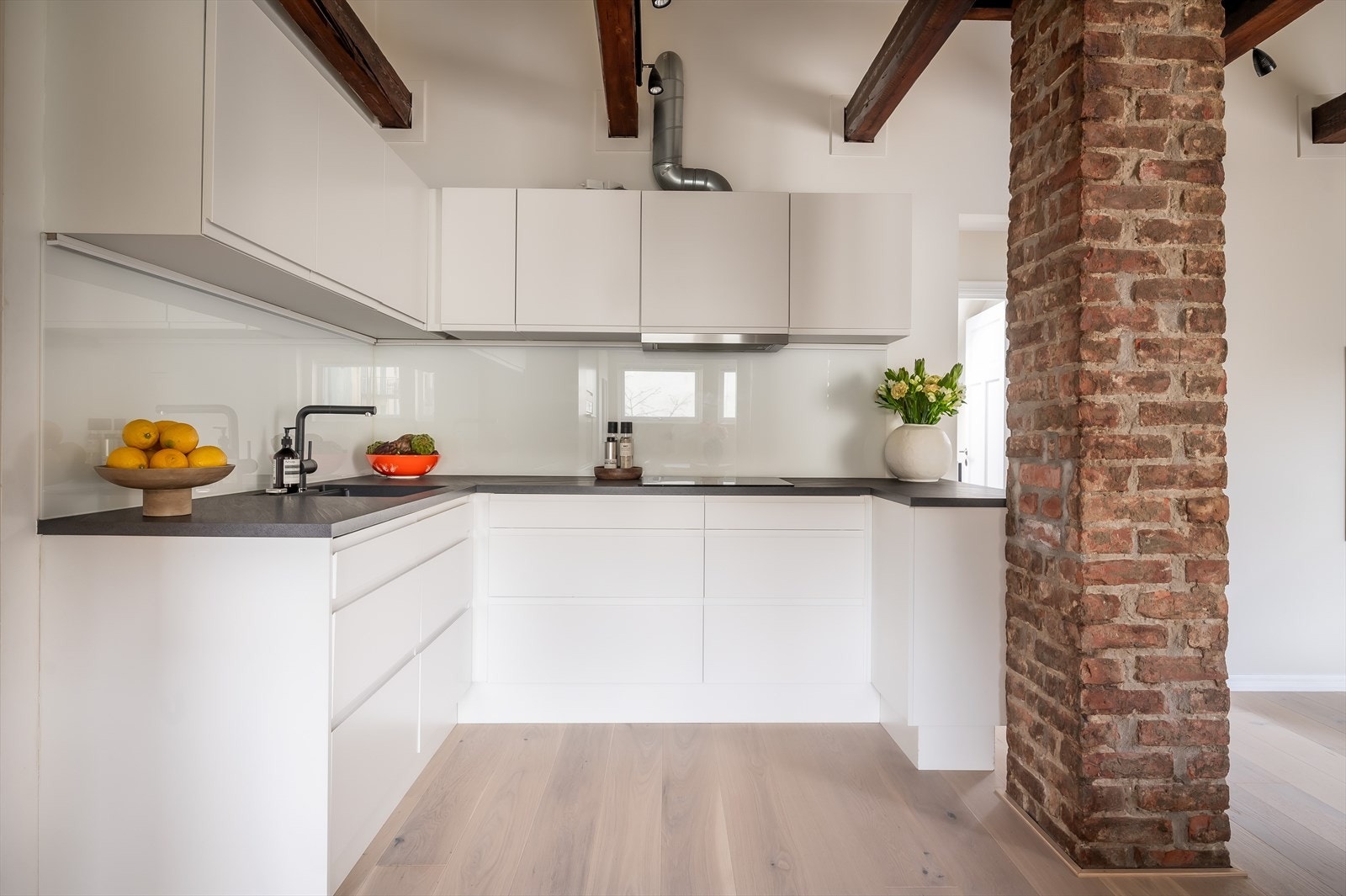 Innredning fra 2019 med hvite, grepsløse fronter, glassplate på vegg over kjøkkenbenk og benkeplate i laminat. Galleribilde