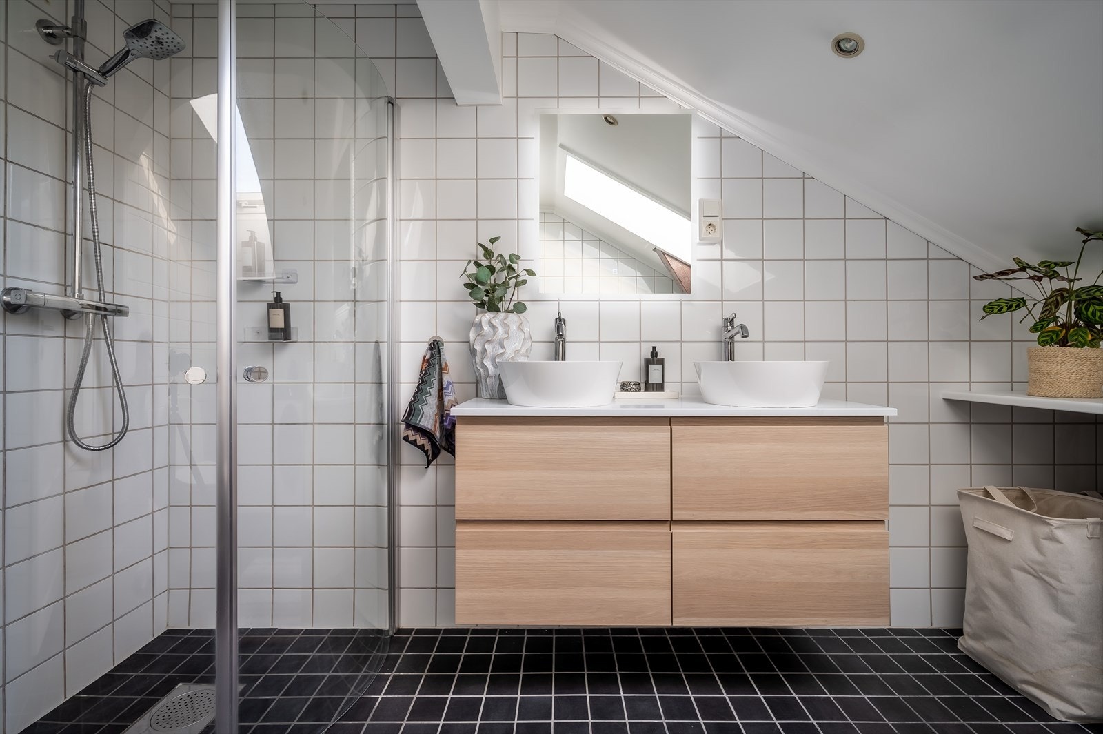 Rommet inneholder dusjnisje med glassvegg, nytt blandebatteri og regnfallsdusj (2023), gulvstående toalett og baderomsinnredning fra 2024 med benk med dobbel servant og skuffer. Galleribilde