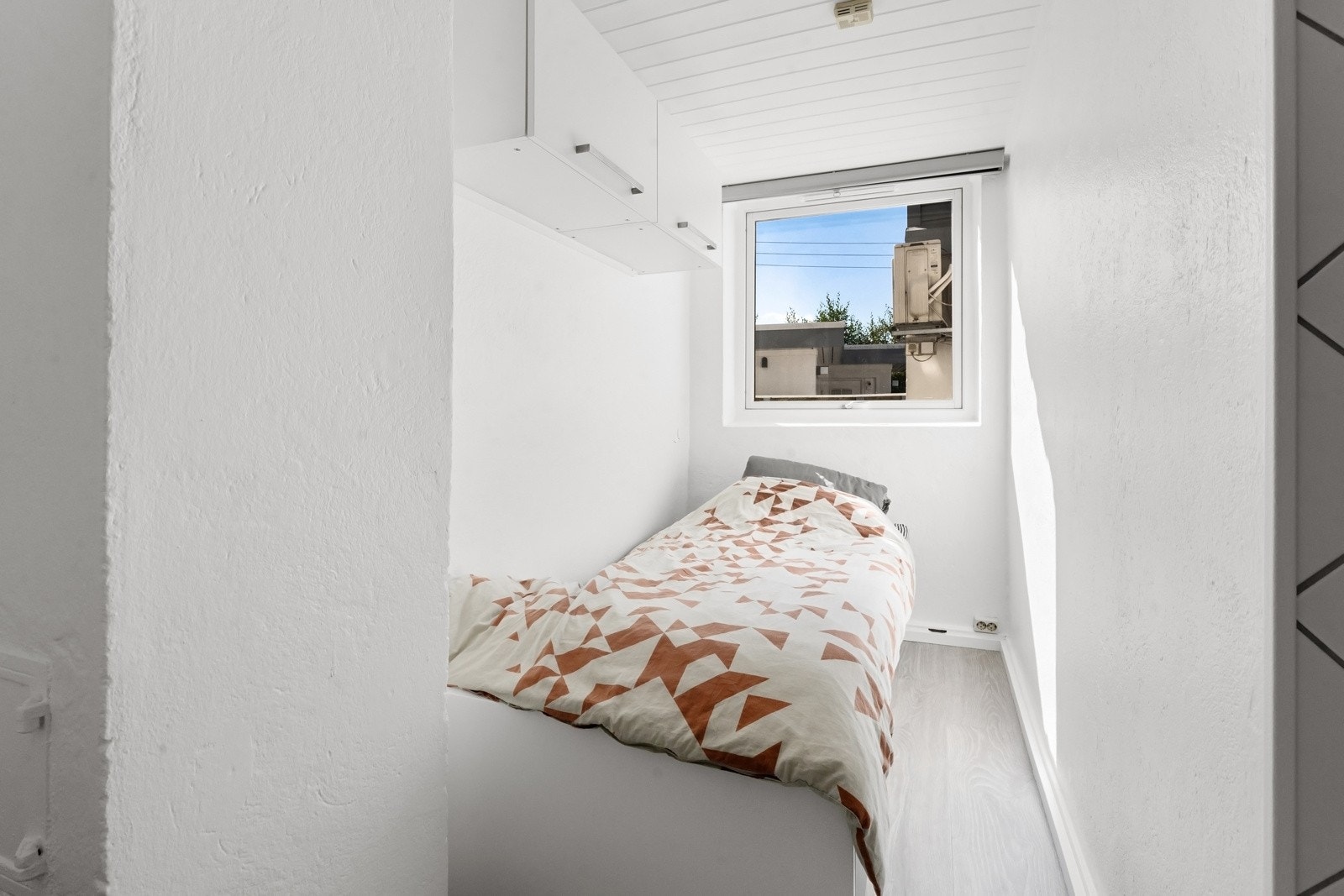 Alkoven har vindu, pent laminatgulv, hvitmalte vegger, hvitmalt panelhimling og veggskap over sengeplassen. Galleribilde