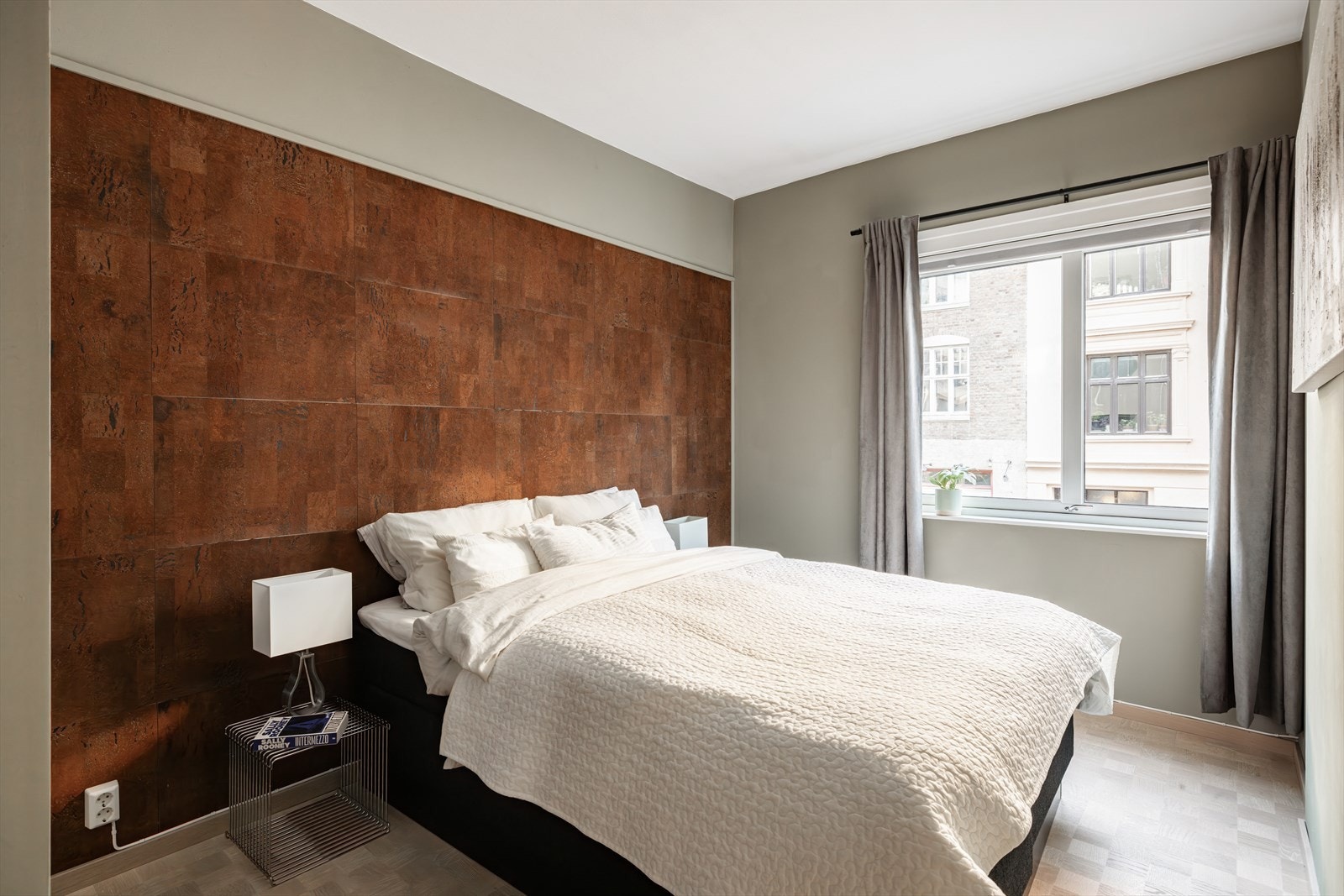 Romslig soverom med parkett i rutemønster på gulv og en vegg er kledd med korkfliser, noe som gir en fin kontrast. Galleribilde