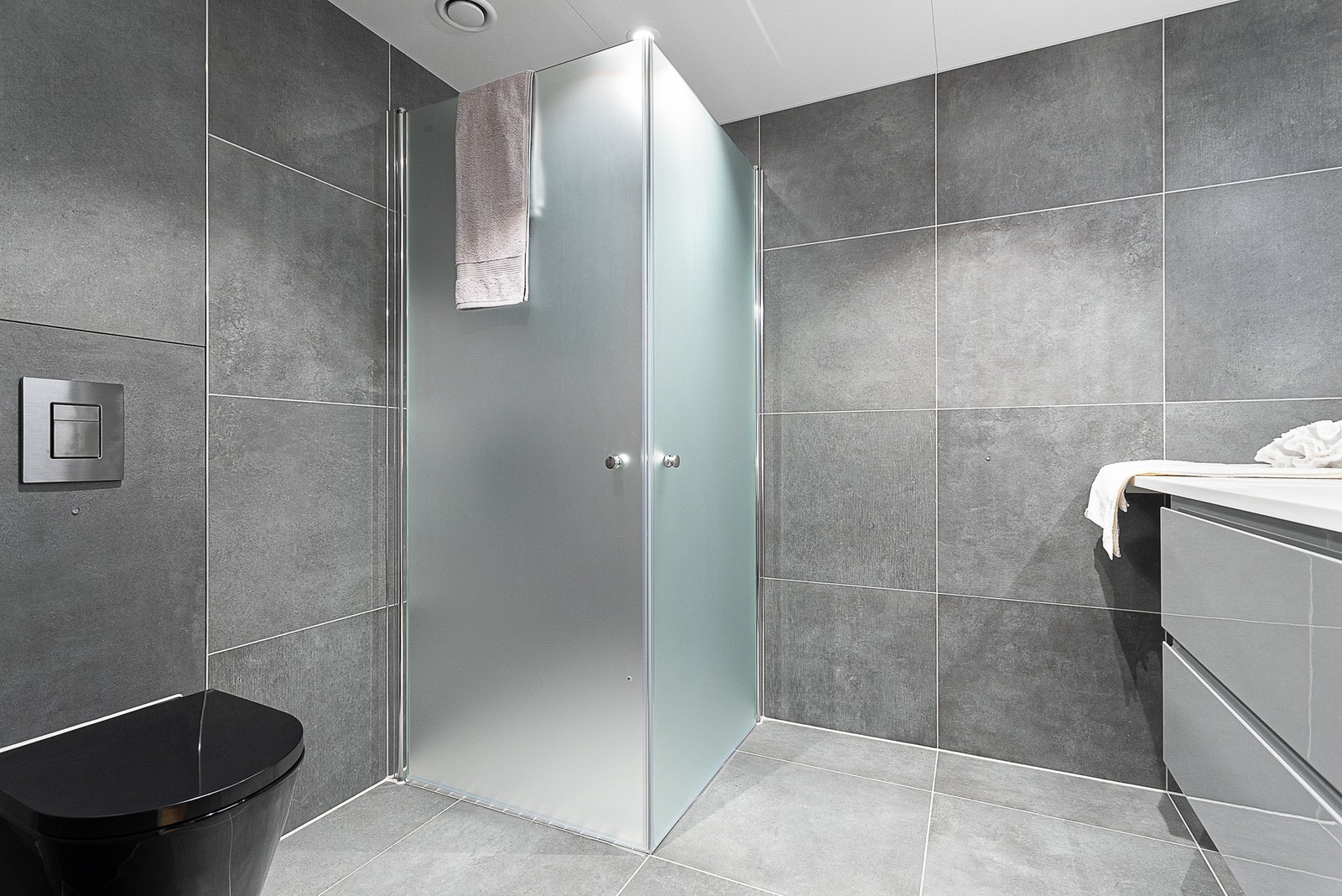 Badet inneholder dusjnisje med innfellbare glassvegger, vegghengt toalett, samt baderomsinnredning med skuffer. Galleribilde