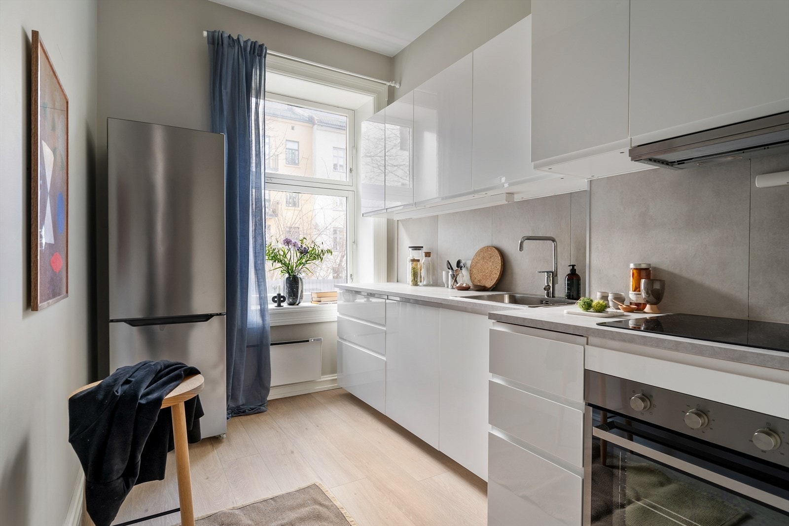 Tidløst kjøkken med en lekker kombinasjon av lyse, slette overflater, integrert grep og grå benkeplate. Galleribilde