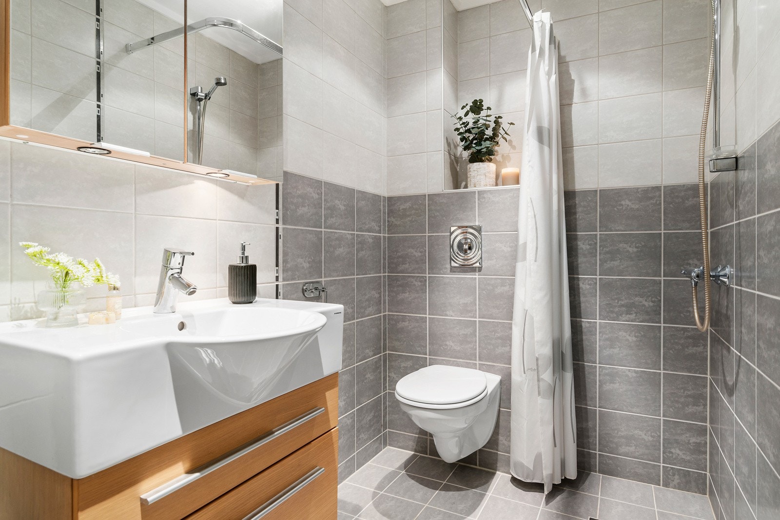 Bad med flis på gulv og vegger. Her er innredning med servant, speilskap, vegghengt toalett og dusj. Galleribilde