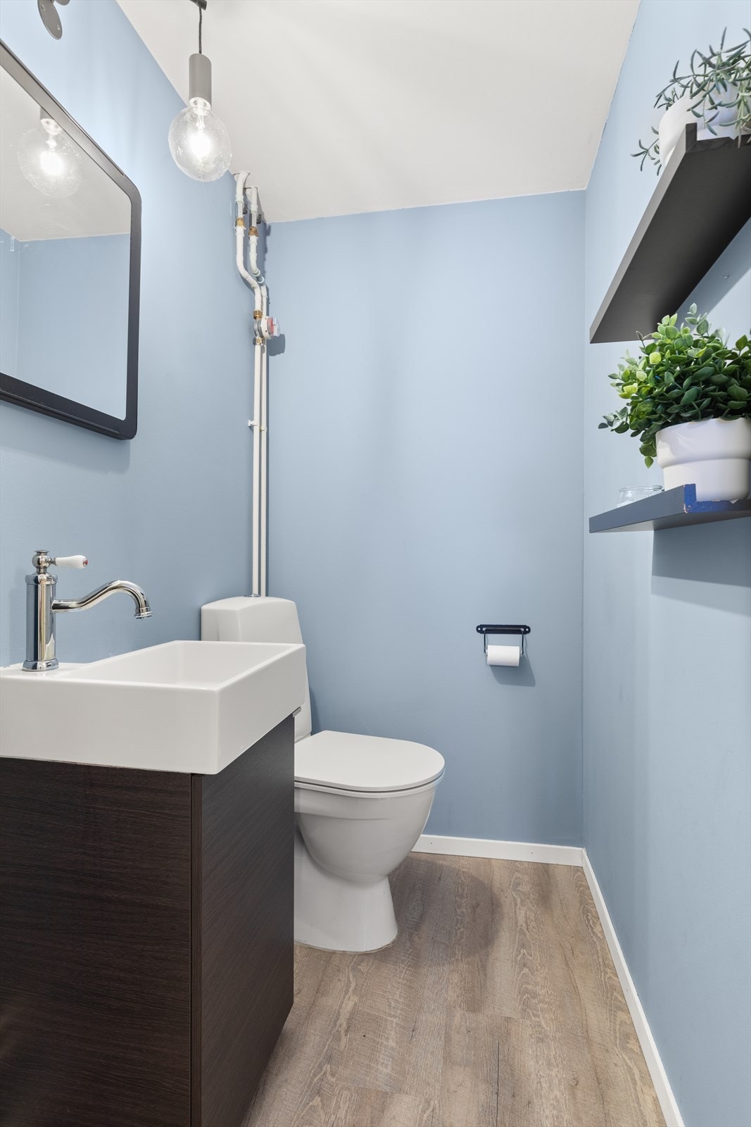 Toalettrom med laminat på gulv, servantseksjon med skap, speil og gulvmontert toalett Galleribilde