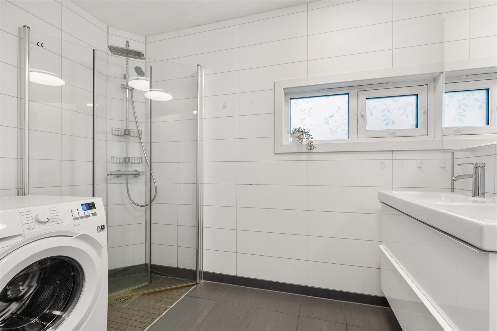 Badet består av dobbel servantseksjon med skuffer, dusjhjørne, overskap med speilfronter og opplegg for vaskemaskin Galleribilde