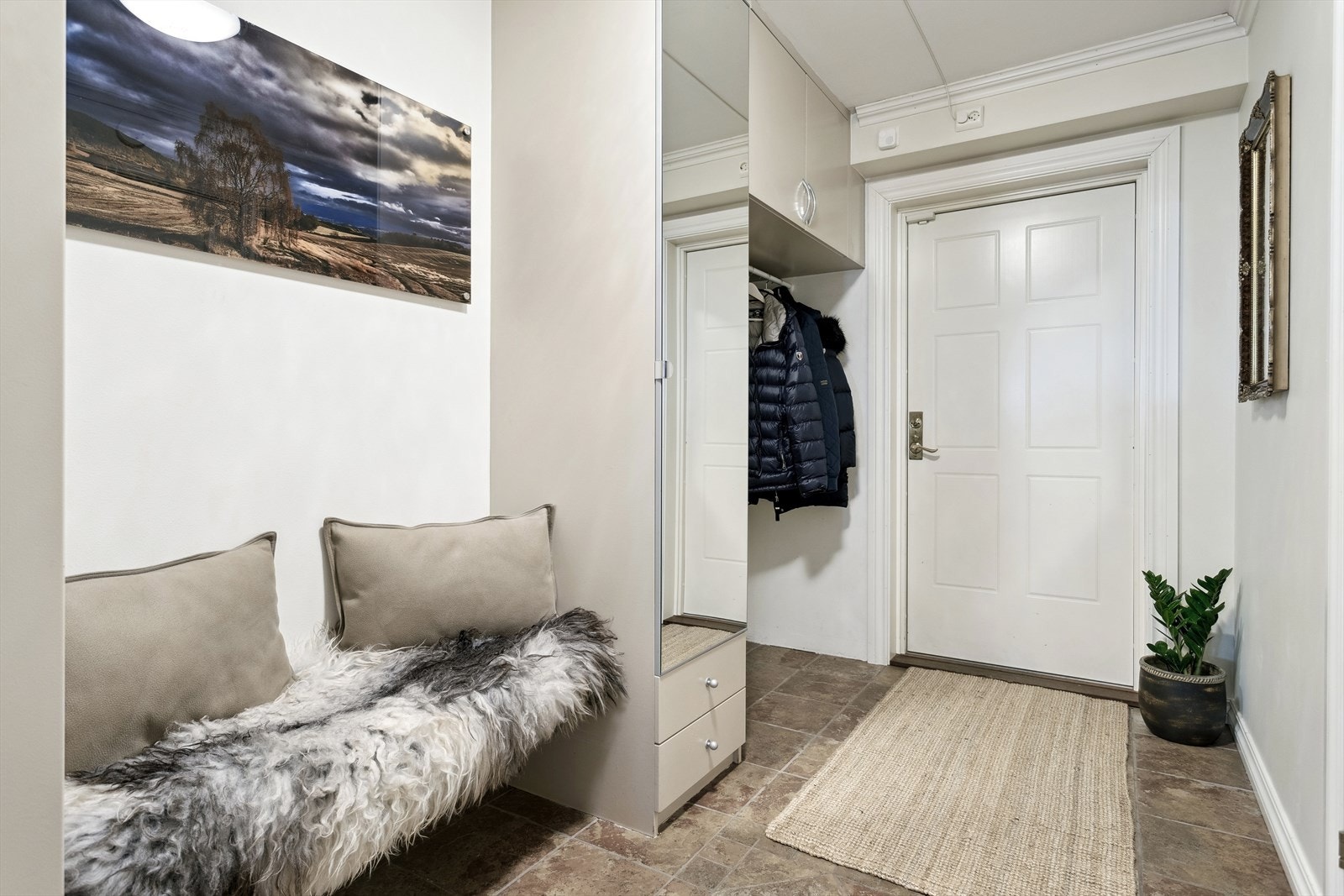 Leiligheten har en romslig og praktisk entré med flislagt gulv med gulvvarm. Her er det allerede plassbygde garderobeskap, som gir gode oppbevaringsmuligheter og bidrar til en ryddig inngangssone. Galleribilde