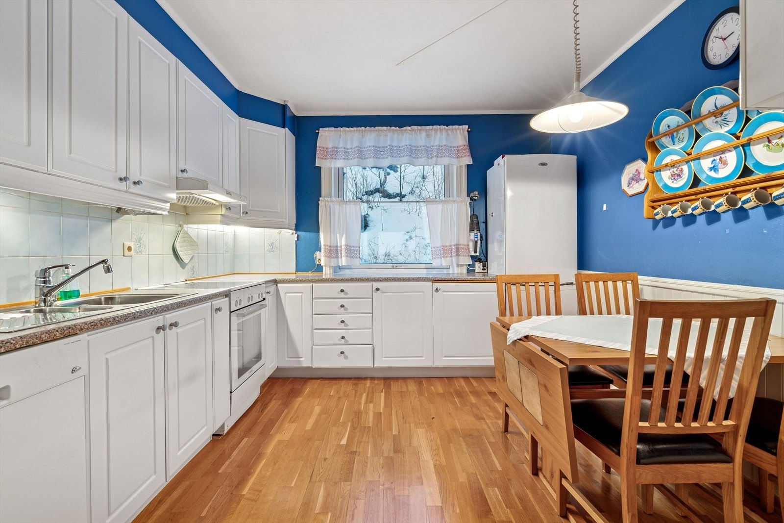 Kjøkkeninnredningen er stilren med hvite profilerte fronter, laminert benkeplate med nedfelt stålvask og fliser på vegg over benk Galleribilde