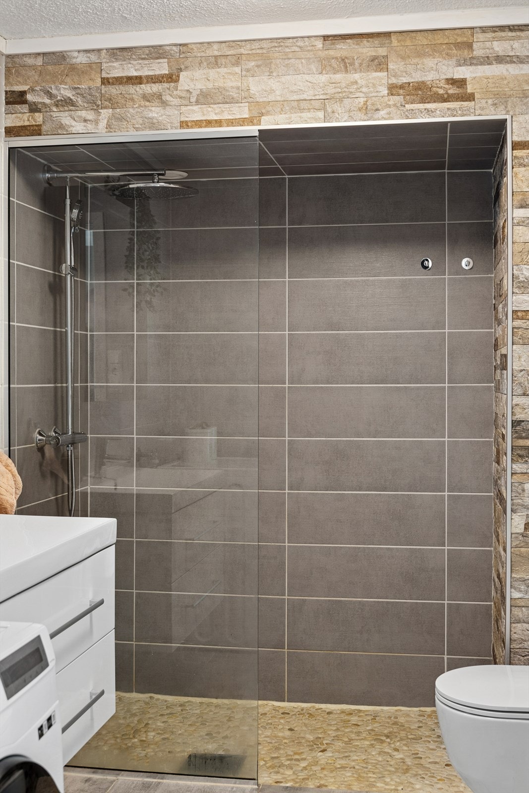 Rommet er utstyrt med veggmontert toalett, dusjløsning med glassvegg, servant, innredning og speil. Opplegg for vaskemaskin. Galleribilde