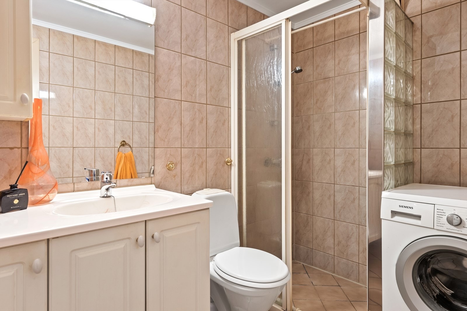 Badet har flislagte overflater, dusjnisje med glassbyggerstein og skyvedør, og opplegg for vaskemaskin. Galleribilde