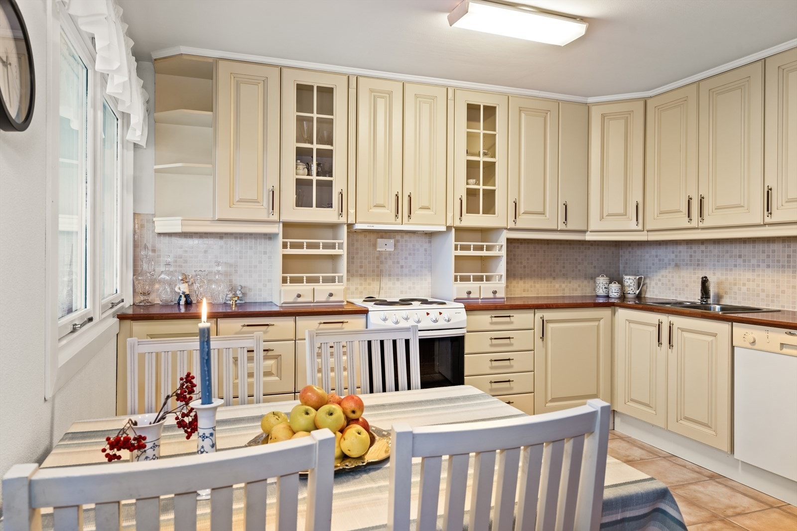 Kjøkkeninnredningen har en funksjonell L-form med over- og underskap i profilerte fronter, vitrineoverskap, hyller og benkeplate i laminat. Galleribilde