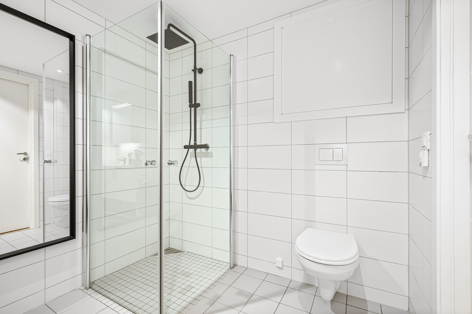 Badet er innredet med dusjhjørne med dusjdører og dusjgarnityr montert på vegg. Vegghengt toalett og baderomsinnredning. Kran og avløp for vaskemaskin. Galleribilde