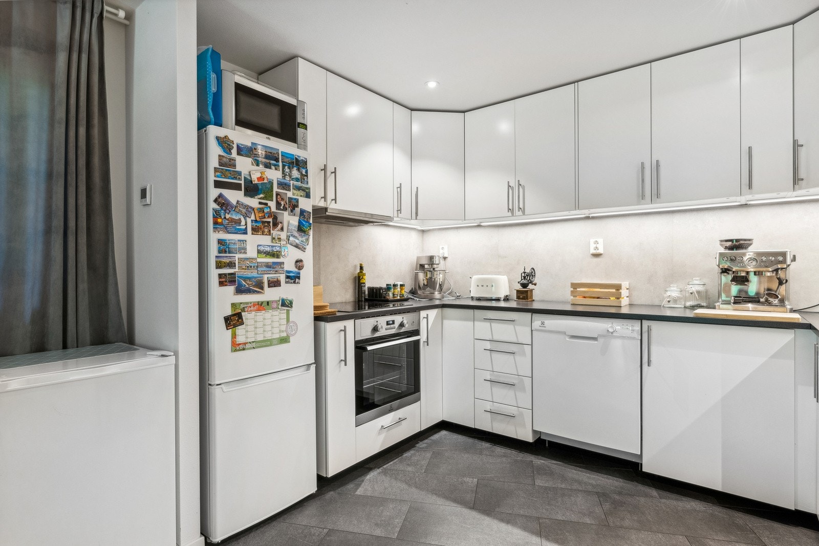 Lys kjøkkeninnredning med glatte fronter, benkeplater i laminat, oppvaskkum med ett-greps blandebatteri og ventilator over kokesonen. Galleribilde