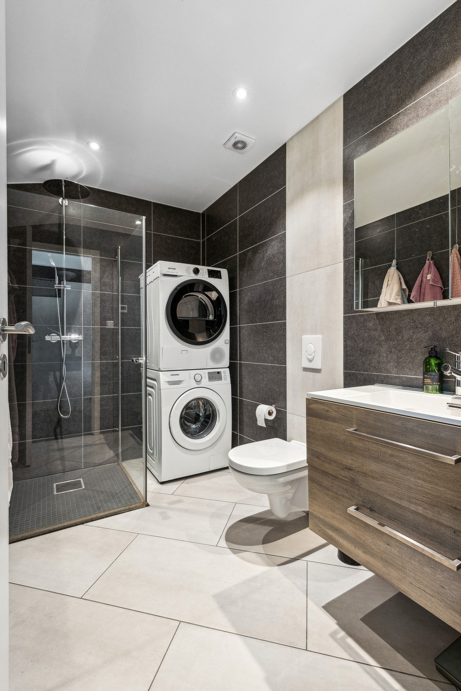 Lekkert baderom fra 2019 med innredning, servant, speil, veggmontert toalett, dusjhjørne og opplegg for vaskemaskin og tørketrommel. Galleribilde