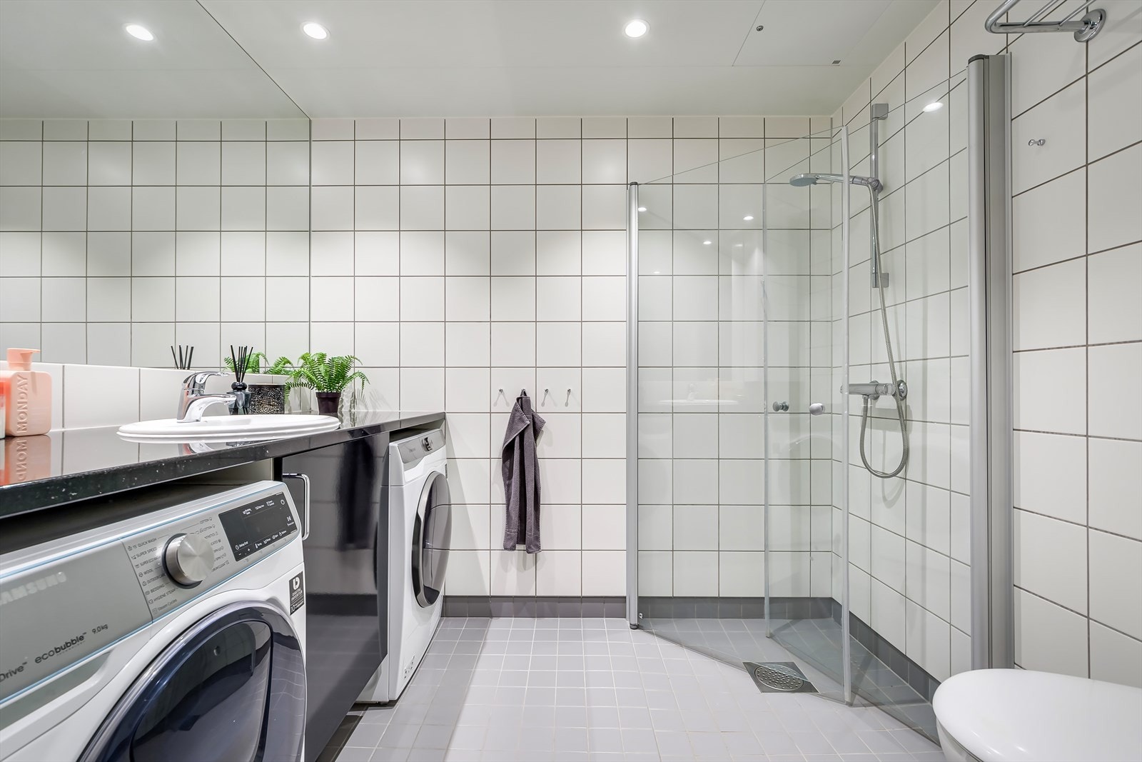 Romslig bad med plass til både vaskemaskin og tørketrommel. Badet har flislagte overflater, behagelig gulvvarme og downlights i taket Galleribilde