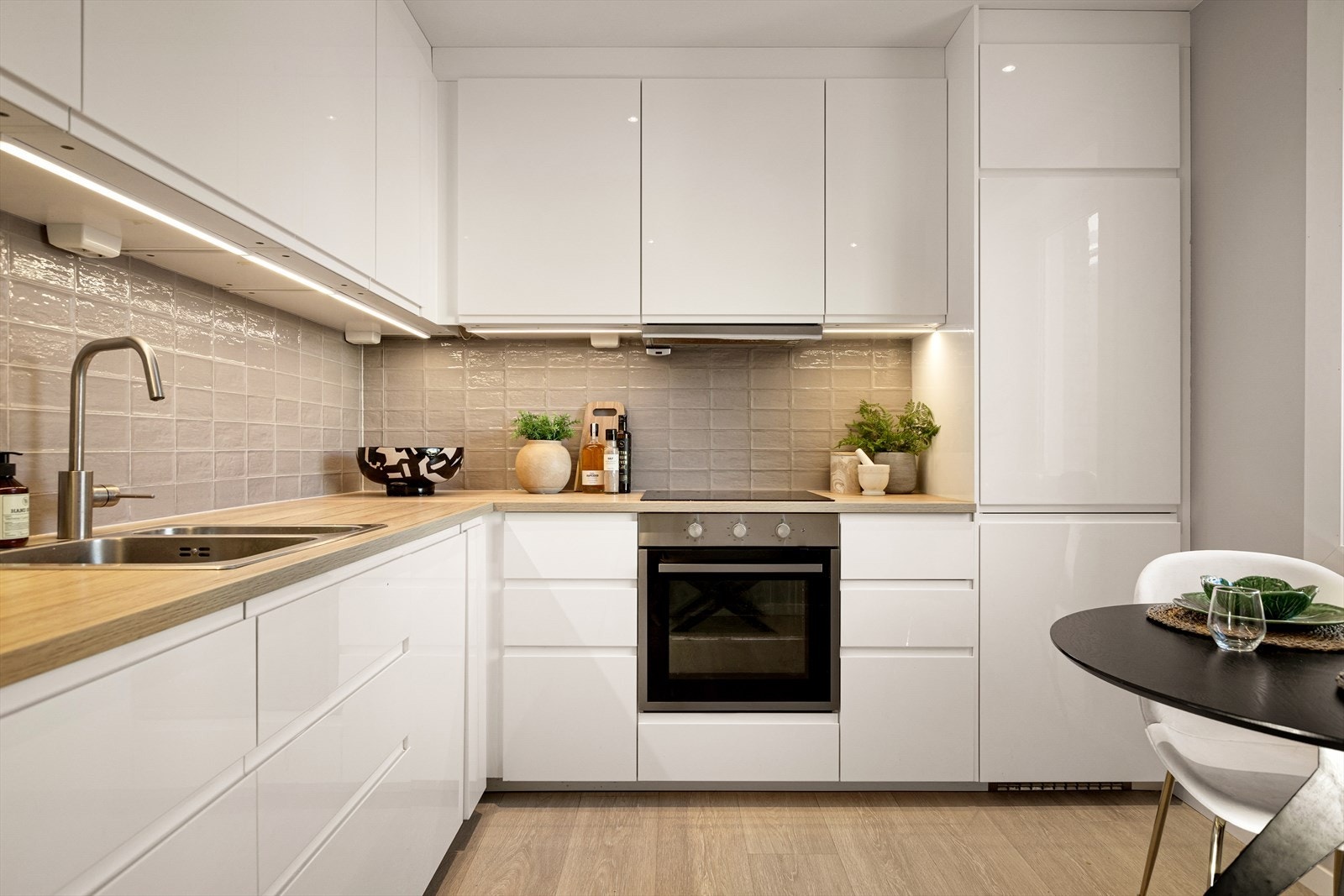 Innredning fra Ikea i 2018/19 med glatte, hvite fronter og laminat benkeplate. Det er flislagt på vegg over kjøkkenbenken. Galleribilde
