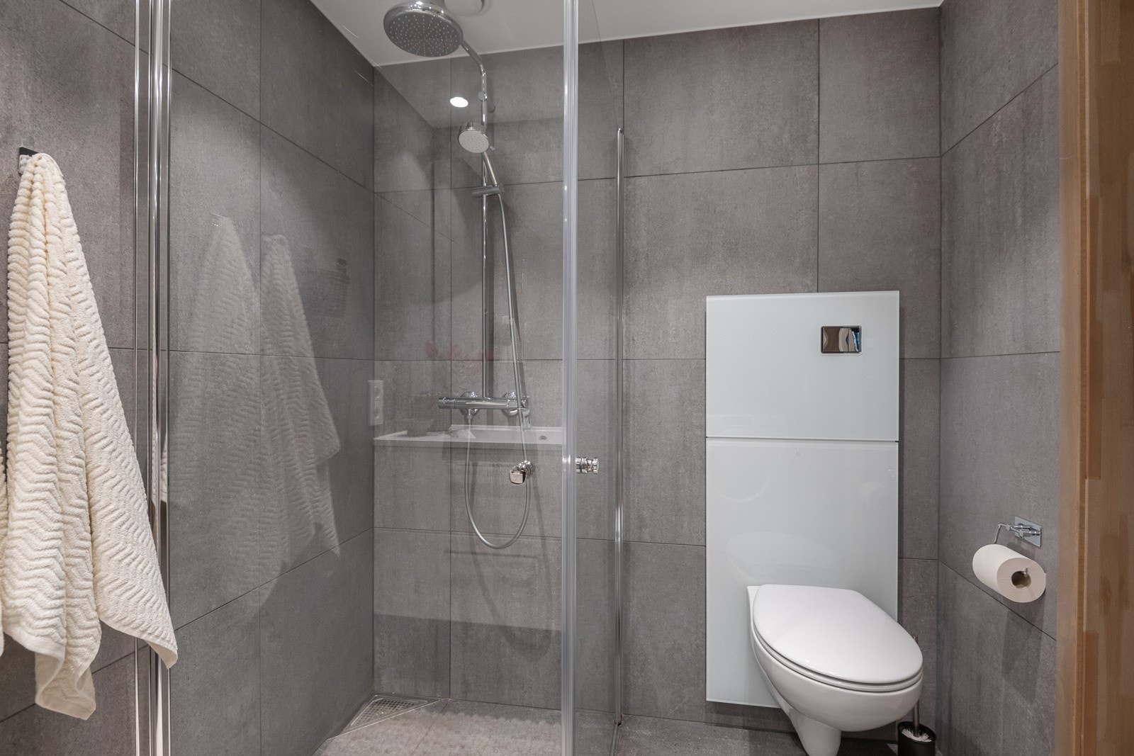 Badet er innredet med servant med underskap, speil med tilhørende belysning, dusjvegger, opplegg for vaskemaskin og vegghengt wc. Galleribilde