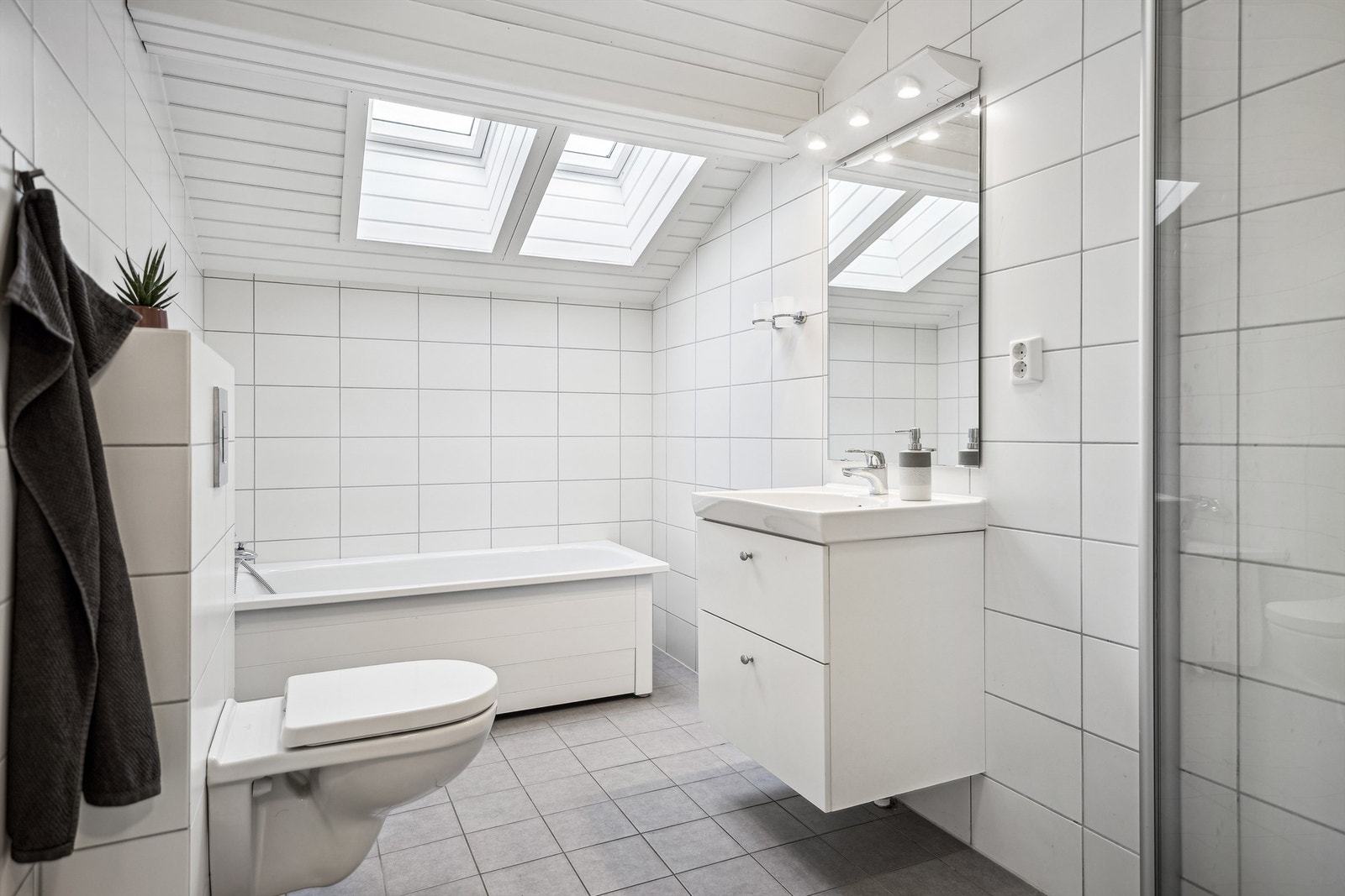 Pent, flislagt bad m/adkomst fra gang med badekar, dusjhjørne med innadslående dører, servant og vegghengt toalett. Galleribilde