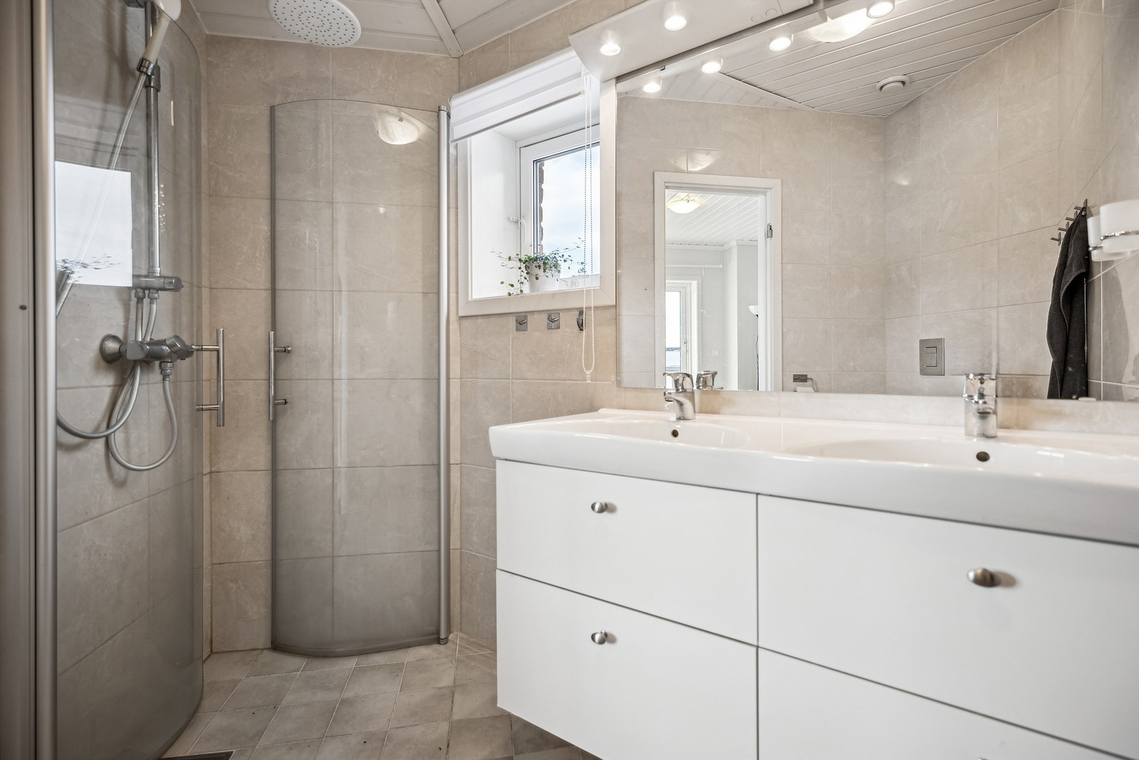 Lekkert, flislagt bad med dusj med innadslående dører, dobbel servant og toalett. Galleribilde