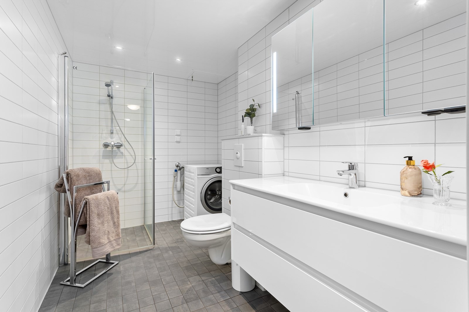 Innredet med dusjhjørne, vegghengt wc, moderne baderomsinnredning og opplegg for vaskemaskin. Galleribilde