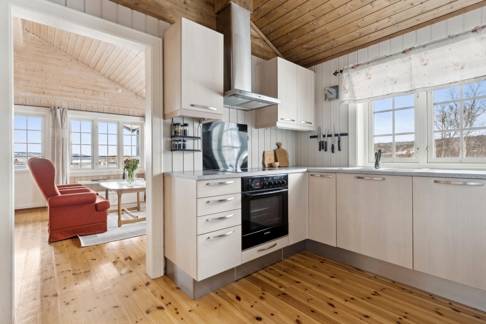 Hvit kjøkkeninnredning med glatte fronter, utstyrt med kjøleskap, koketopp og stekovn. Galleribilde